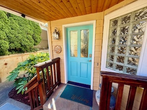 A blue door with a glass panel, a wooden porch railing, a welcome mat, and a wall-mounted sign.