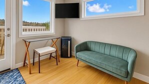 A room with a green sofa, a small table, a chair, a TV mounted on the wall, and large windows with a view of the outdoors. - 180° Space Needle, Lake Union & Downtown Views! (Seattle)