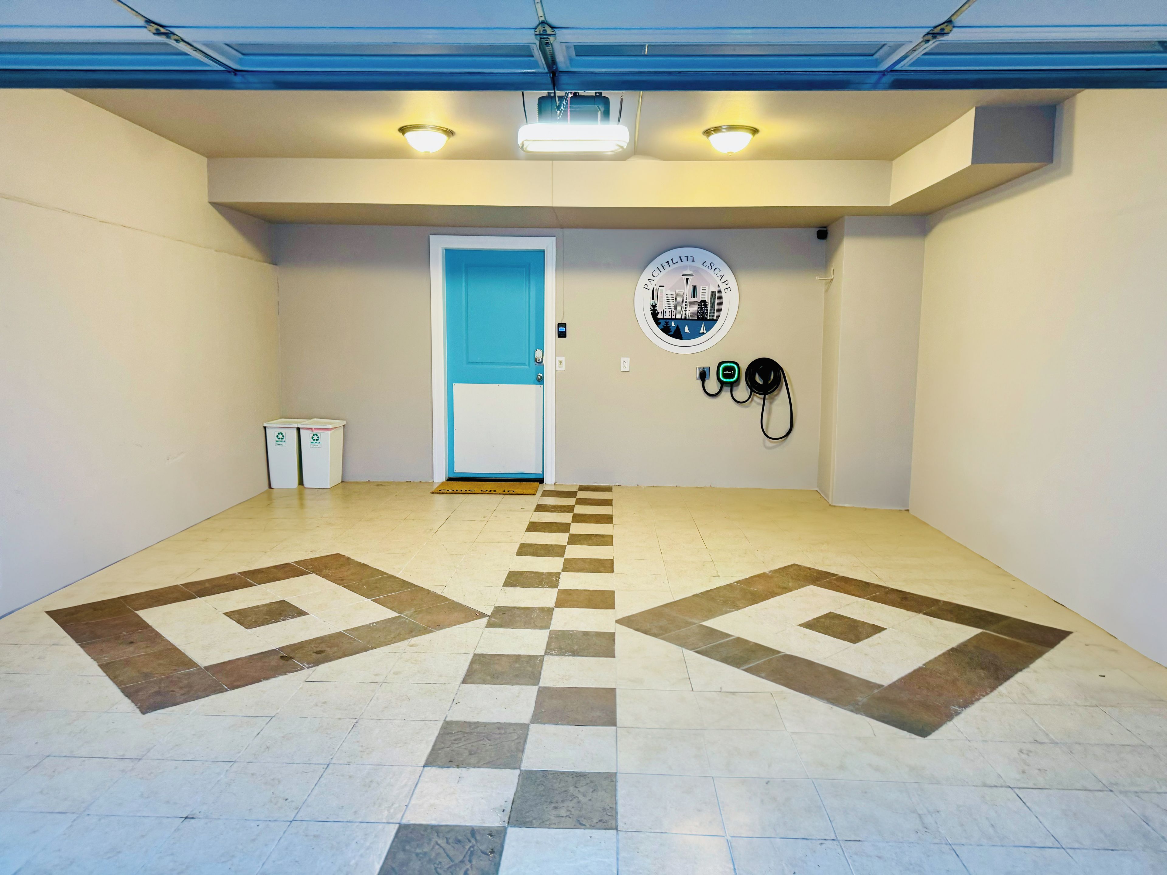 Un espace intérieur propre et bien éclairé, avec un sol à carreaux, une porte bleue, une poubelle de recyclage et une borne de recharge fixée au mur.