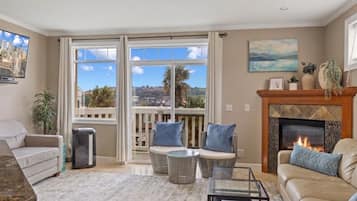 A living room with a fireplace, a sofa, a coffee table, and a view of a cityscape through large windows.