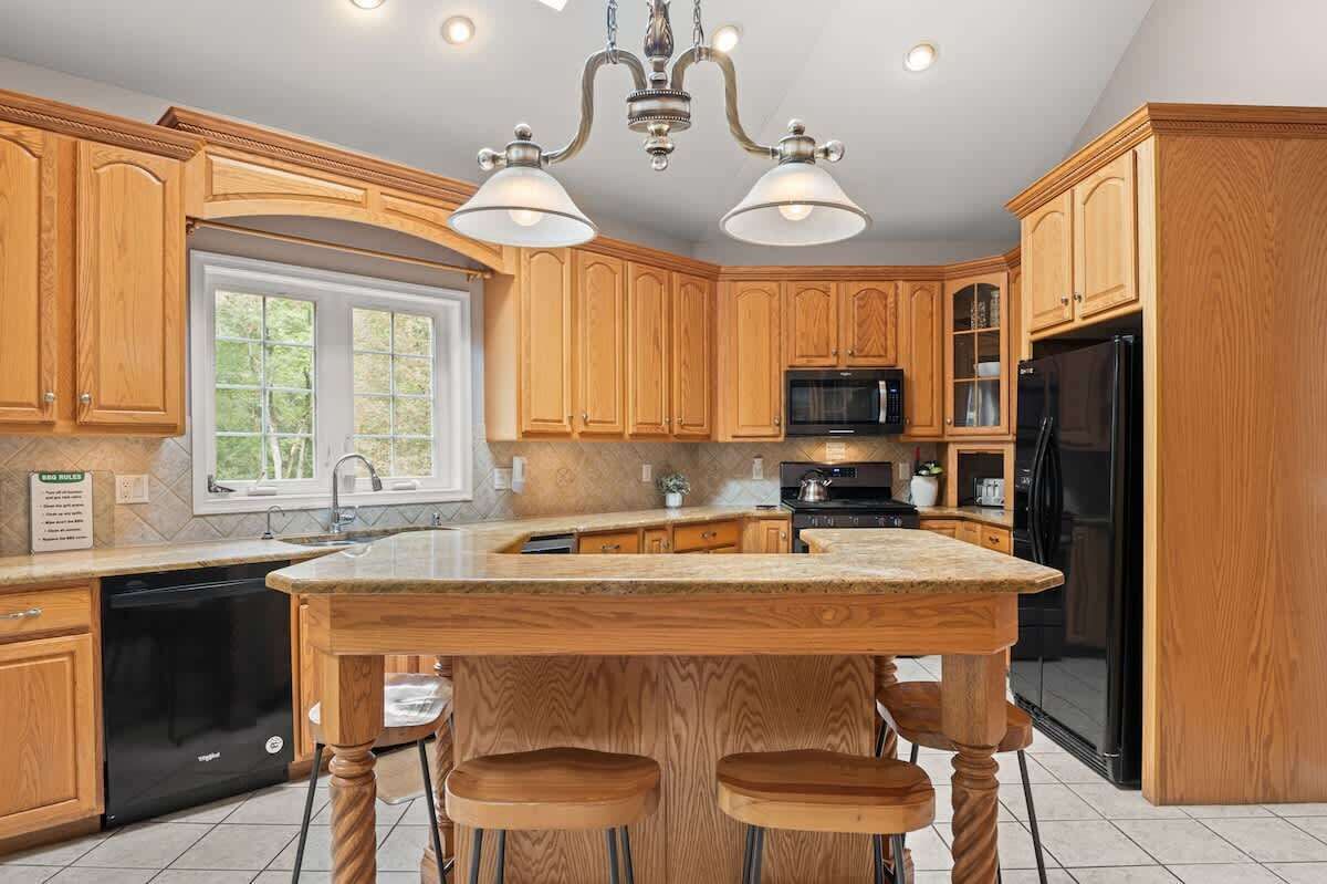 A kitchen with wooden cabinets, a black refrigerator, a microwave, and a large island with stools.
