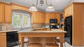 A kitchen with wooden cabinets, a black refrigerator, a microwave, and a large island with stools.