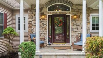 A house with a stone facade, a dark front door with a floral wreath, and two wicker chairs on the porch.