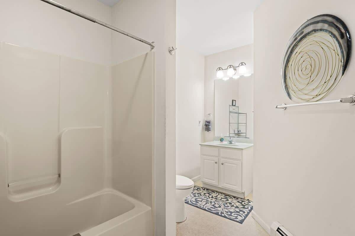 A bathroom with a shower, toilet, vanity, and a decorative wall piece.