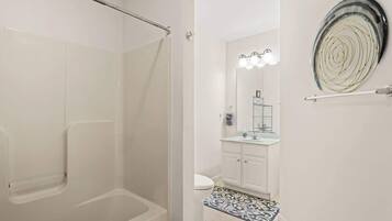 A bathroom with a shower, toilet, vanity, and a decorative wall piece.