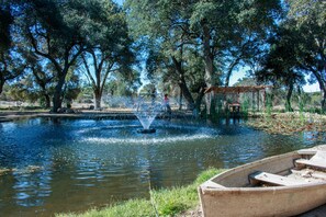 A wooden boat docked at a calm pond with a fountain in the center, surrounded by trees. - Secluded rental on 40 acre ranch. (Warner Springs)