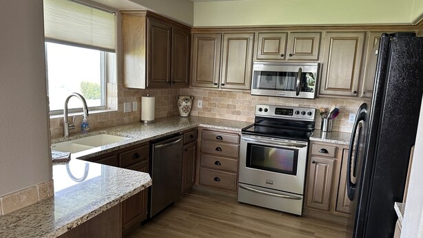 Una cocina con armarios de madera, horno de acero inoxidable, microondas, lavavajillas y refrigerador.