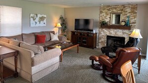 Una sala de estar con sofá, mesa de centro, televisor, chimenea y sillón de cuero.