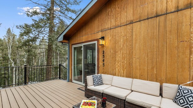 A wooden deck with a wicker sofa and a table with a fruit platter and two mugs. - Bear Paw Haven-nestled in the trees. Pet & family friendly. HOT TUB, Free WiFi (Woodland Park)