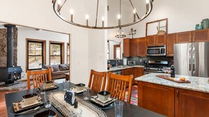 A modern kitchen with wooden cabinets, stainless steel appliances, and a dining area with a large table set for six. - Bear Paw Haven-nestled in the trees. Pet & family friendly. HOT TUB, Free WiFi (Woodland Park)