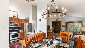 A modern kitchen with stainless steel appliances, wooden cabinets, and a dining area with a large table and chairs. - Bear Paw Haven-nestled in the trees. Pet & family friendly. HOT TUB, Free WiFi (Woodland Park)