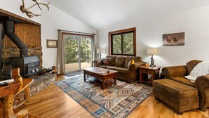 A living room with a stone fireplace, wooden furniture, and a large window. - Bear Paw Haven-nestled in the trees. Pet & family friendly. HOT TUB, Free WiFi (Woodland Park)