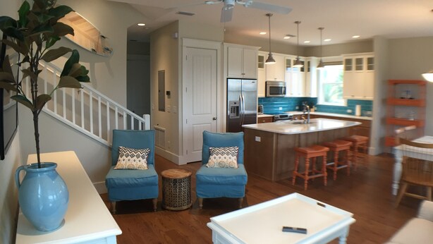A modern kitchen with a central island, a dining area with blue chairs, and a living room with a coffee table and blue sofa. - Steps to the non-driving section of the beach!  (Saint Augustine Beach)