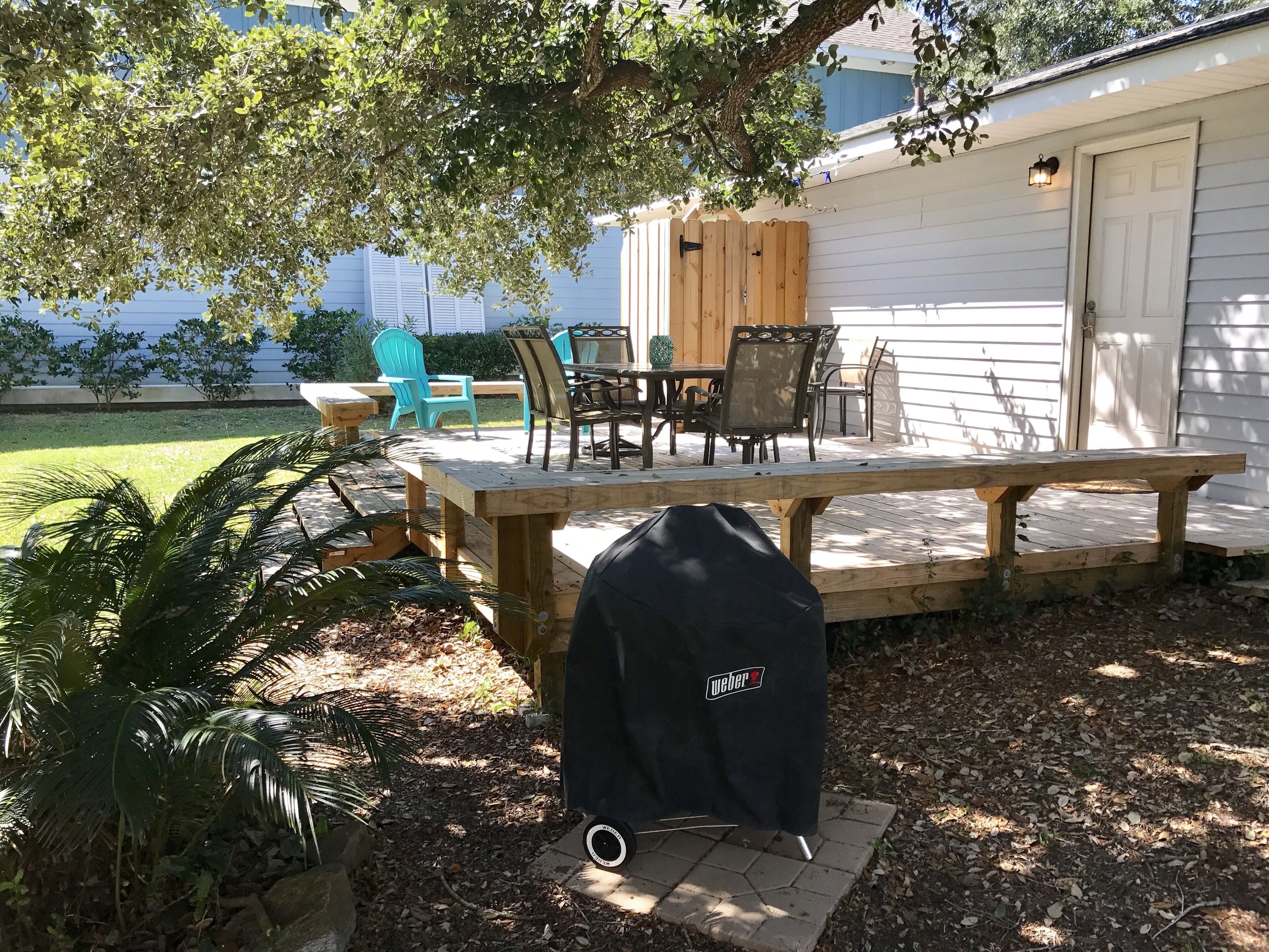 Eine Holzterrasse mit Gartenmöbeln, einem Grill und einem Gartenhaus.