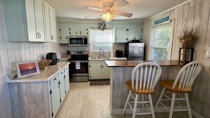 Une cuisine avec des meubles de couleur bleu clair, un four à micro-ondes, une cuisinière, un réfrigérateur et deux chaises blanches.
