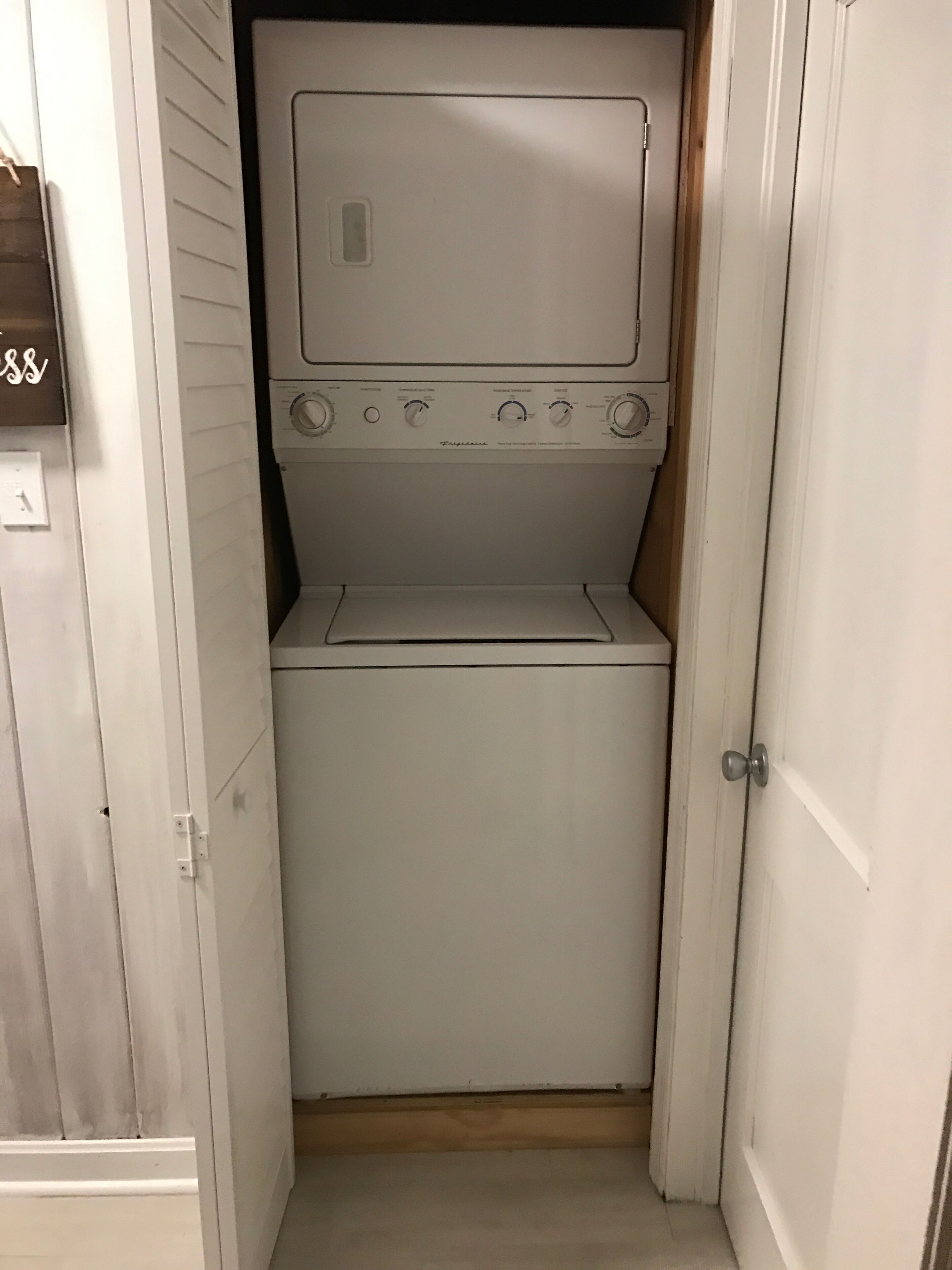 A compact, white laundry room with a front-loading washing machine and dryer, a small window, and a door with a silver handle.