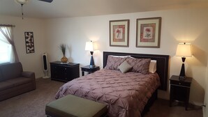 A bedroom with a bed, two bedside tables with lamps, a dresser, a chair, and a radiator.