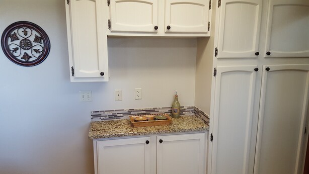 A kitchen with white cabinets, a granite countertop, a decorative wall plate, and a bottle on the counter.