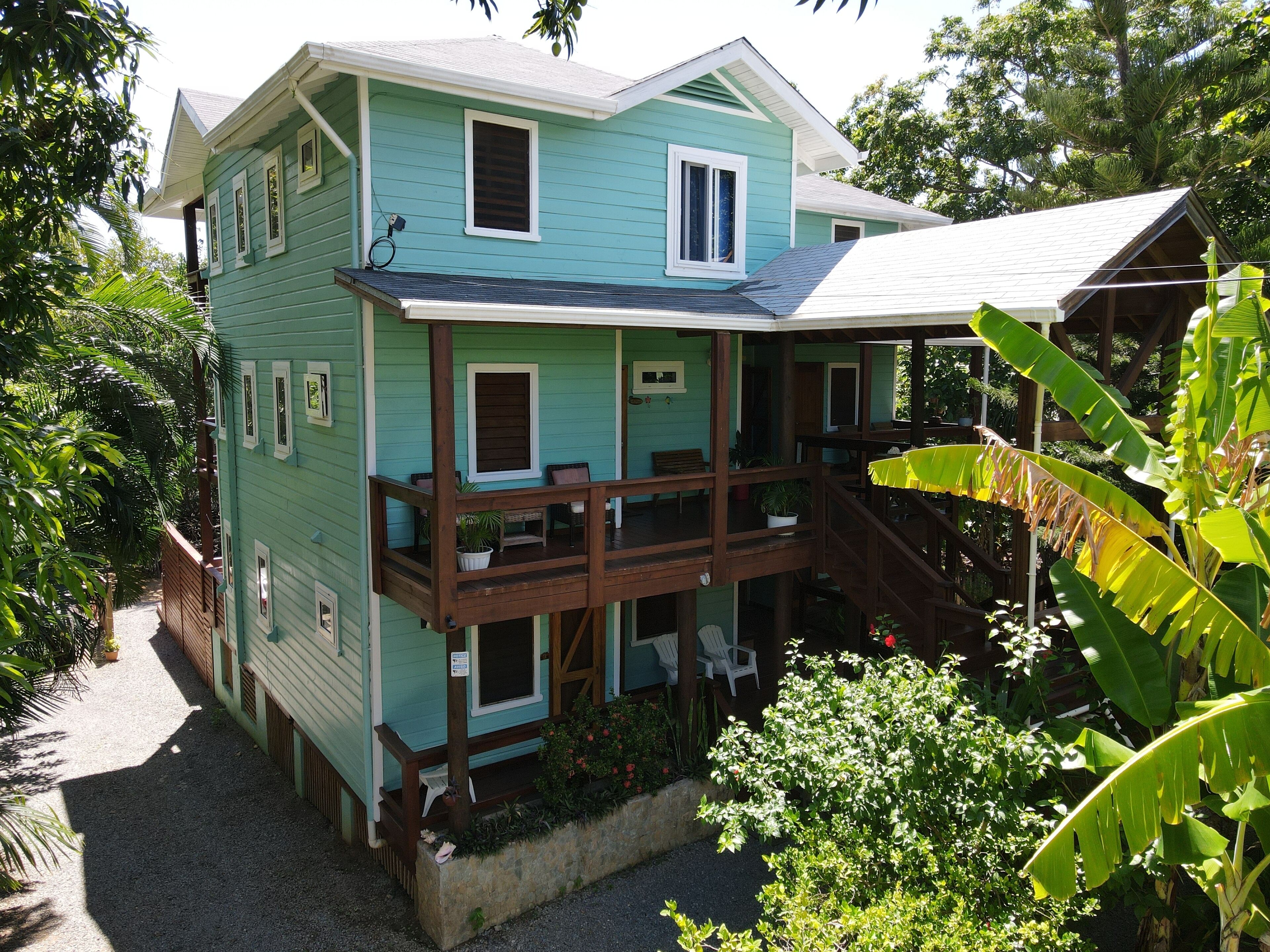 Une maison à deux étages dotée d’un balcon, entourée d’une végétation luxuriante.