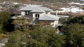 Una casa moderna con techo de metal, rodeada de árboles frondosos y un lago.