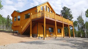 A two-story log cabin with a balcony, a staircase, and a gravel driveway. - Secluded mountain cabin in the woods (Jefferson)
