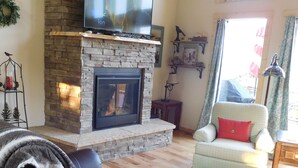 A living room with a stone fireplace, leather sofa, and a television mounted above the fireplace. - Secluded mountain cabin in the woods (Jefferson)