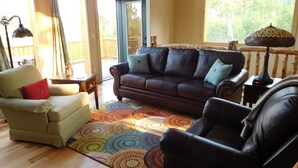 A living room with a brown leather sofa, a beige armchair, and a black leather chair. There is a colorful circular rug on the floor. - Secluded mountain cabin in the woods (Jefferson)