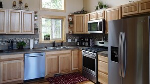 A modern kitchen with wooden cabinets, stainless steel appliances, a dishwasher, and a large window providing natural light. - Secluded mountain cabin in the woods (Jefferson)