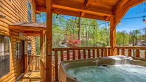 A wooden cabin with a hot tub on the porch, surrounded by trees and a clear sky. - Wooded Cabin · Private Hot Tub · Pet-Friendly · Near Pigeon Forge (Sevierville)