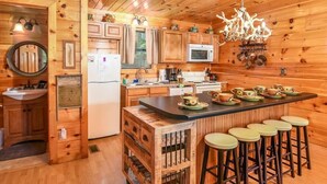 A wooden cabin kitchen with a central island, bar stools, a refrigerator, a microwave, and wooden cabinets. - Wooded Cabin · Private Hot Tub · Pet-Friendly · Near Pigeon Forge (Sevierville)