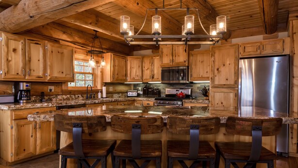 A rustic kitchen with wooden cabinets, a stainless steel refrigerator, and a bar area with wooden stools. - Fabulous Log Home - 2 Master Bedrooms! (Tabernash)