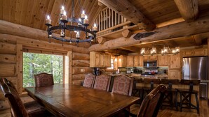 A wooden cabin interior with a dining table, chairs, a chandelier, and a kitchen area. - Fabulous Log Home - 2 Master Bedrooms! (Tabernash)