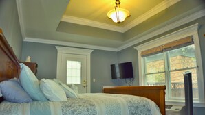 Un dormitorio con una cama, un televisor montado en la pared y una ventana con vistas al exterior.
