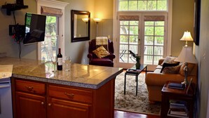 Una cocina con encimera de granito, armarios de madera y una botella de vino. Hay un rincón comedor con un sofá y una lámpara.
