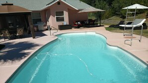 En swimmingpool med springbræt, liggestole og grillområde.