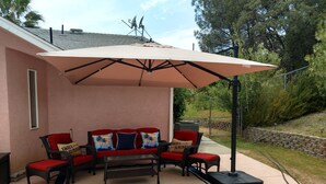 En terrasse med en rød sofa, en beige parasol og en stenvæg i baggrunden.