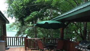 A wooden deck with outdoor seating, a grill, and a view of a lake.
