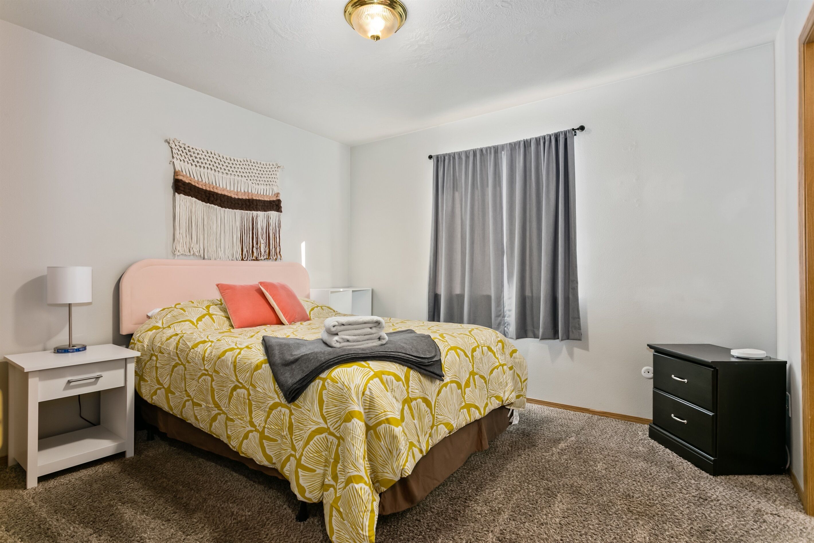 A neatly arranged bedroom with a bed, bedside tables, a wall tapestry, and a window with curtains.