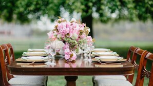 A dining table set for six with a floral centerpiece, surrounded by wooden chairs.