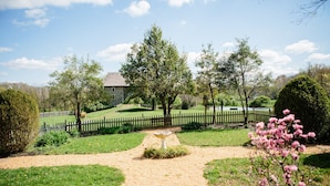 A garden pathway leading to a stone building with a fenced area and a pond.