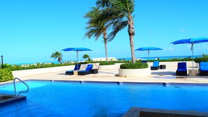 Un espace piscine doté de chaises longues et de parasols, offrant une vue dégagée sur l’océan, et une piscine bien entretenue.