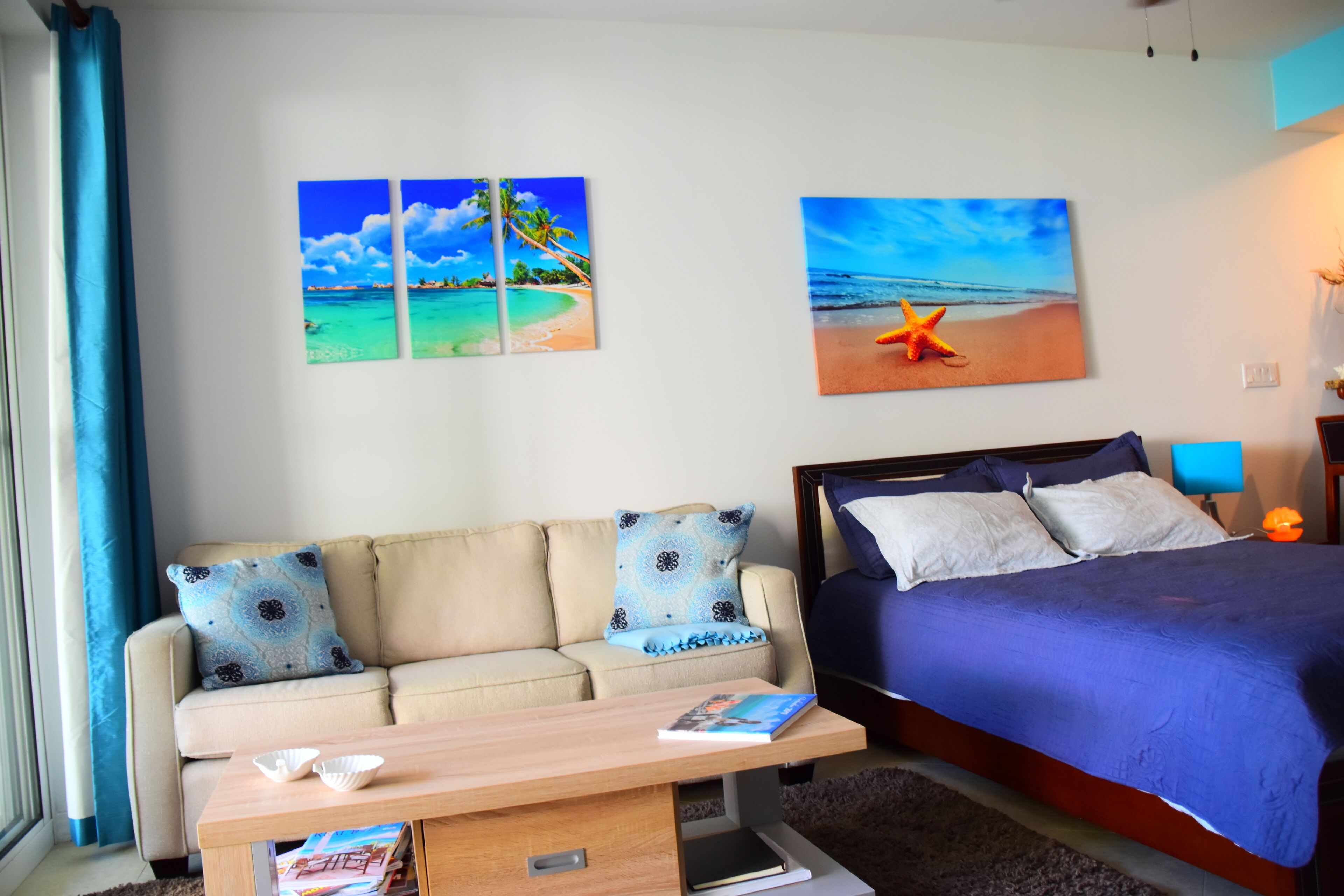 Een slaapkamer met een bed, een bank en twee wanddecoraties met afbeeldingen van het strand.