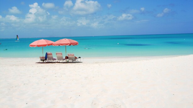 Une plage de sable blanc, avec une eau turquoise et limpide, et quelques parasols qui offrent de l’ombre.