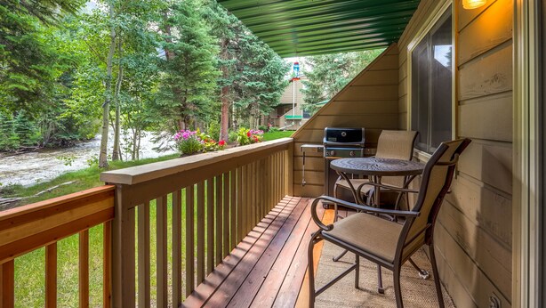 Une terrasse en bois avec un barbecue et des chaises, donnant sur une rivière et des arbres.