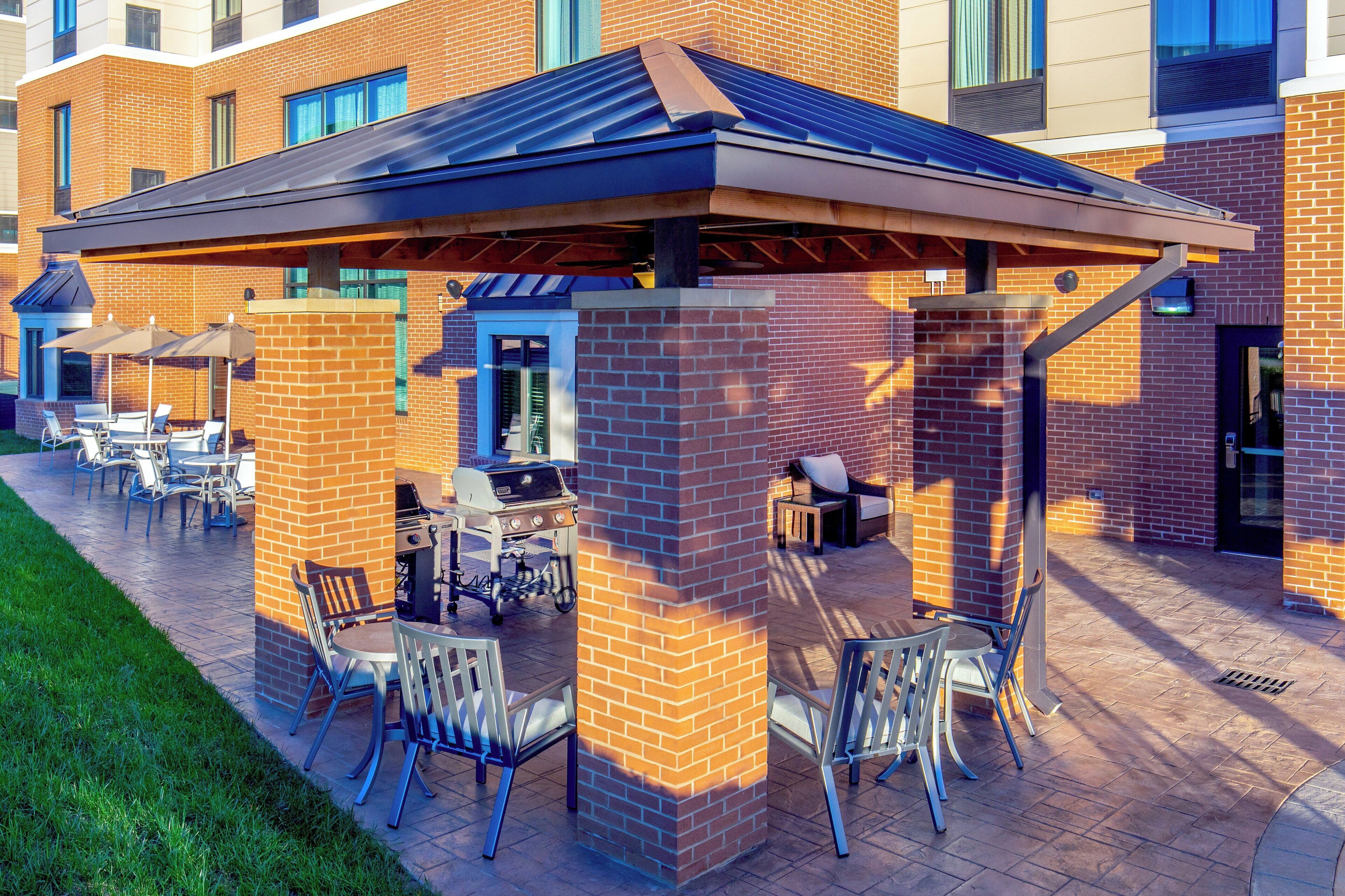 An outdoor patio area with brick pillars, metal chairs, and a grill station.