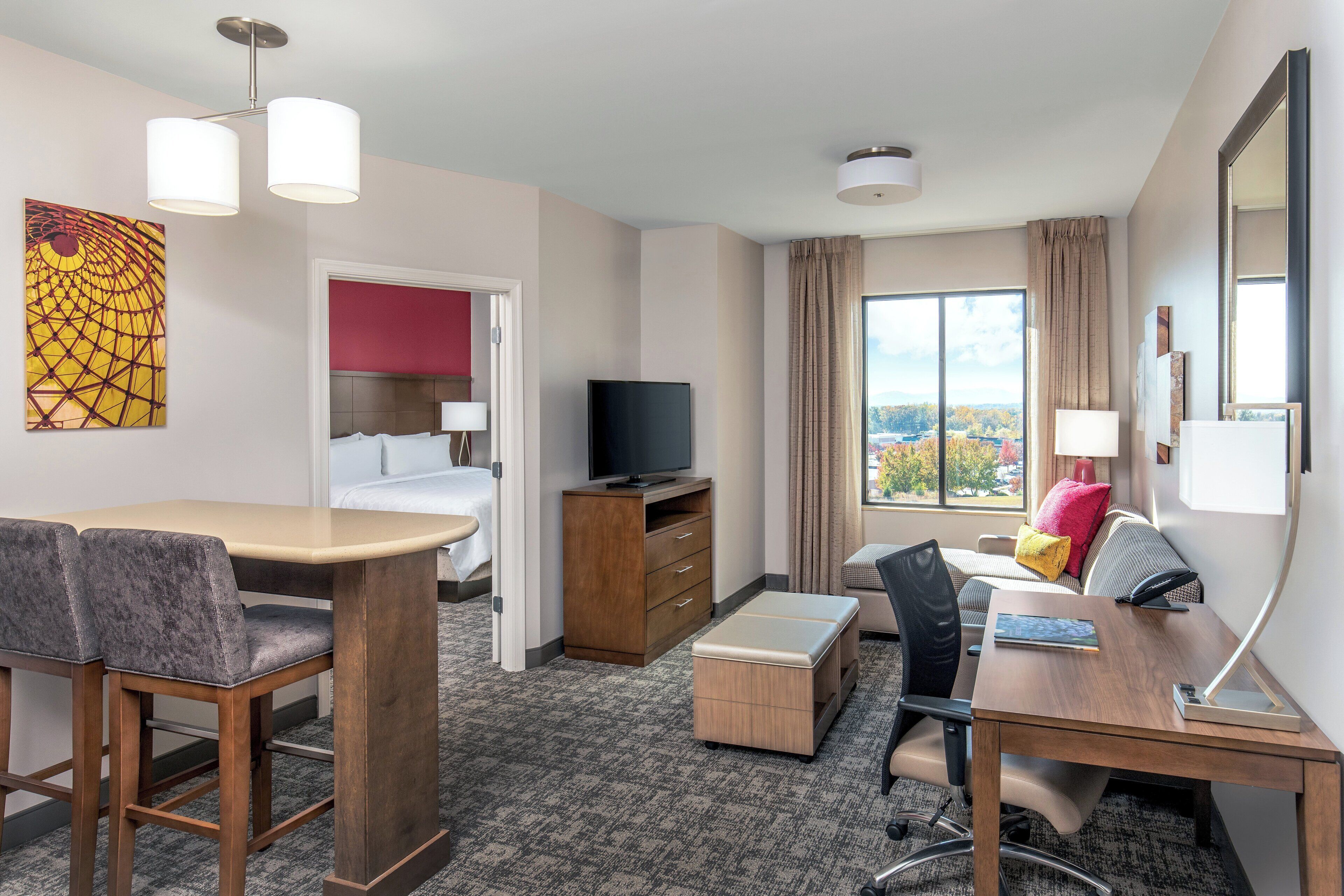 A hotel room with a bed, a desk, a television, and a view of the outdoors.