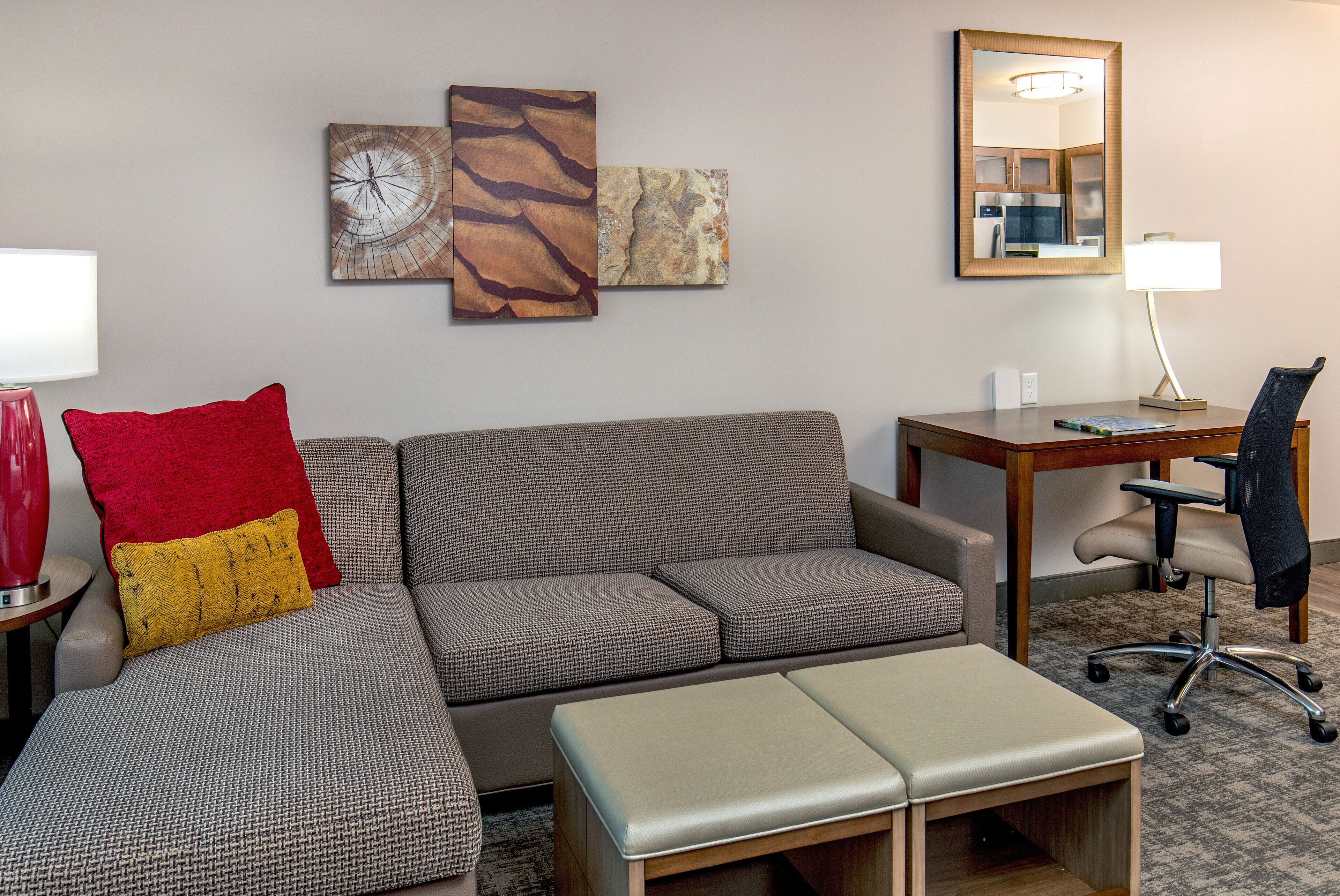 A modern living room with a sectional sofa, a small table, a desk, and a chair. There are two wall art pieces above the sofa.