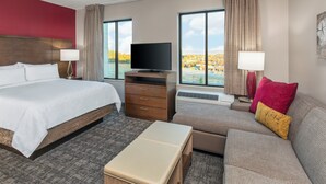 A hotel room with a large bed, a TV, a sofa, and a view of a lake. - Staybridge Suites Charlottesville Airport by IHG (Charlottesville)