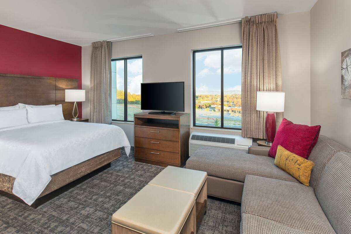 Une chambre d’hôtel avec un grand lit, une télévision, un canapé et une vue sur un lac.