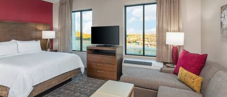 A hotel room with a large bed, a TV, a sofa, and a view of a lake.